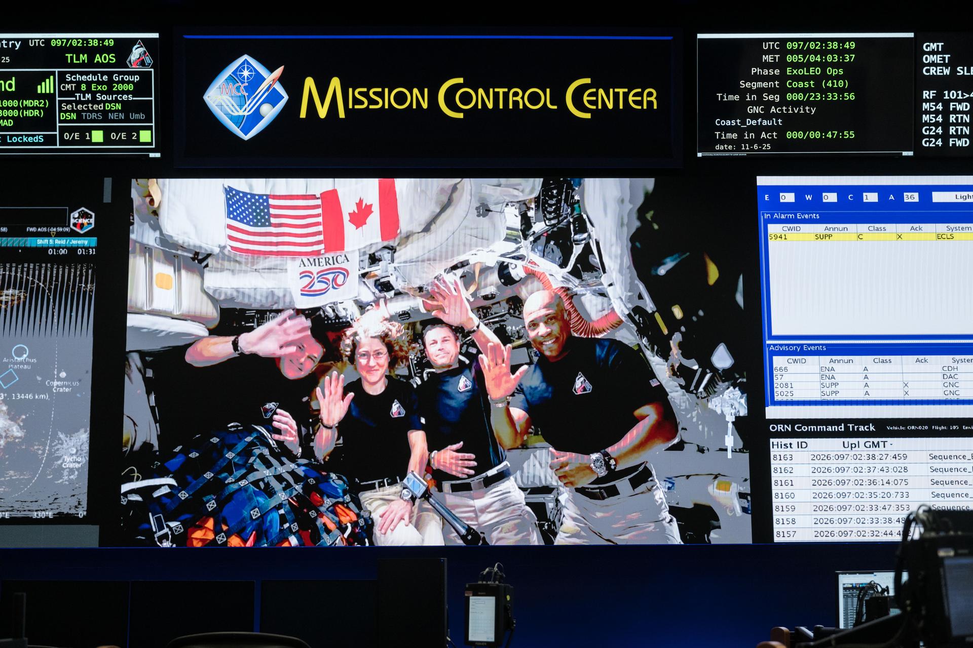 Mission Control Center screen displaying Artemis II crew waving inside Orion capsule after lunar flyby
