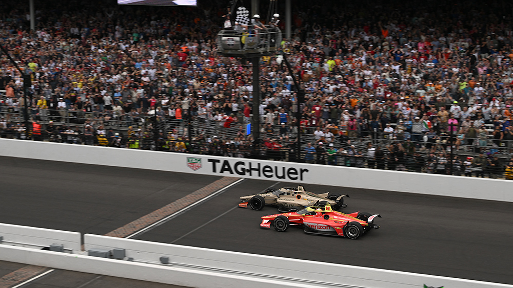 Two IndyCar cars cross the finish line side by side at Indianapolis Motor Speedway